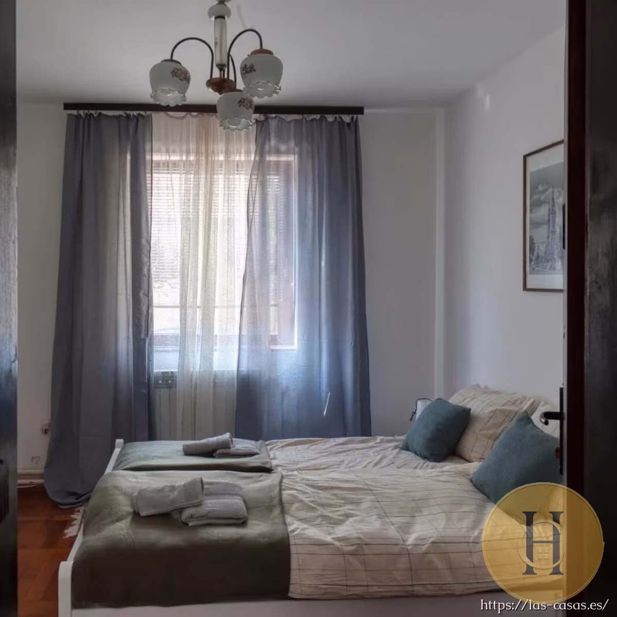 Habitación doble con cama compartida, cortinas grises, lámpara vintage y toallas dispuestas sobre las camas.