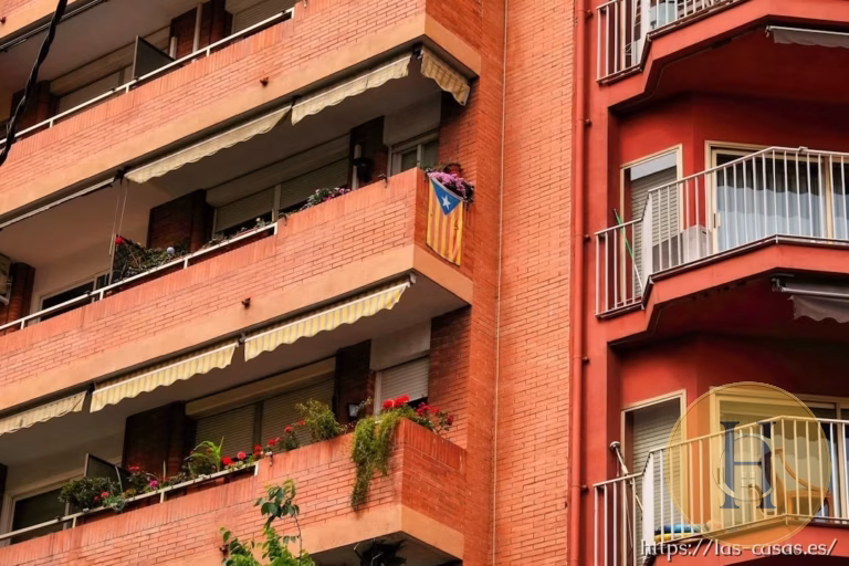 Fachada de edificio residencial con balcones, plantas y una bandera estelada colgada en uno de ellos