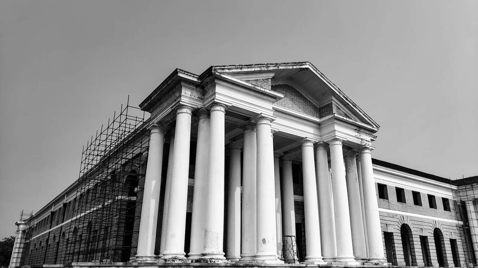 Fachada neoclásica con columnas y andamios de obra, en blanco y negro.