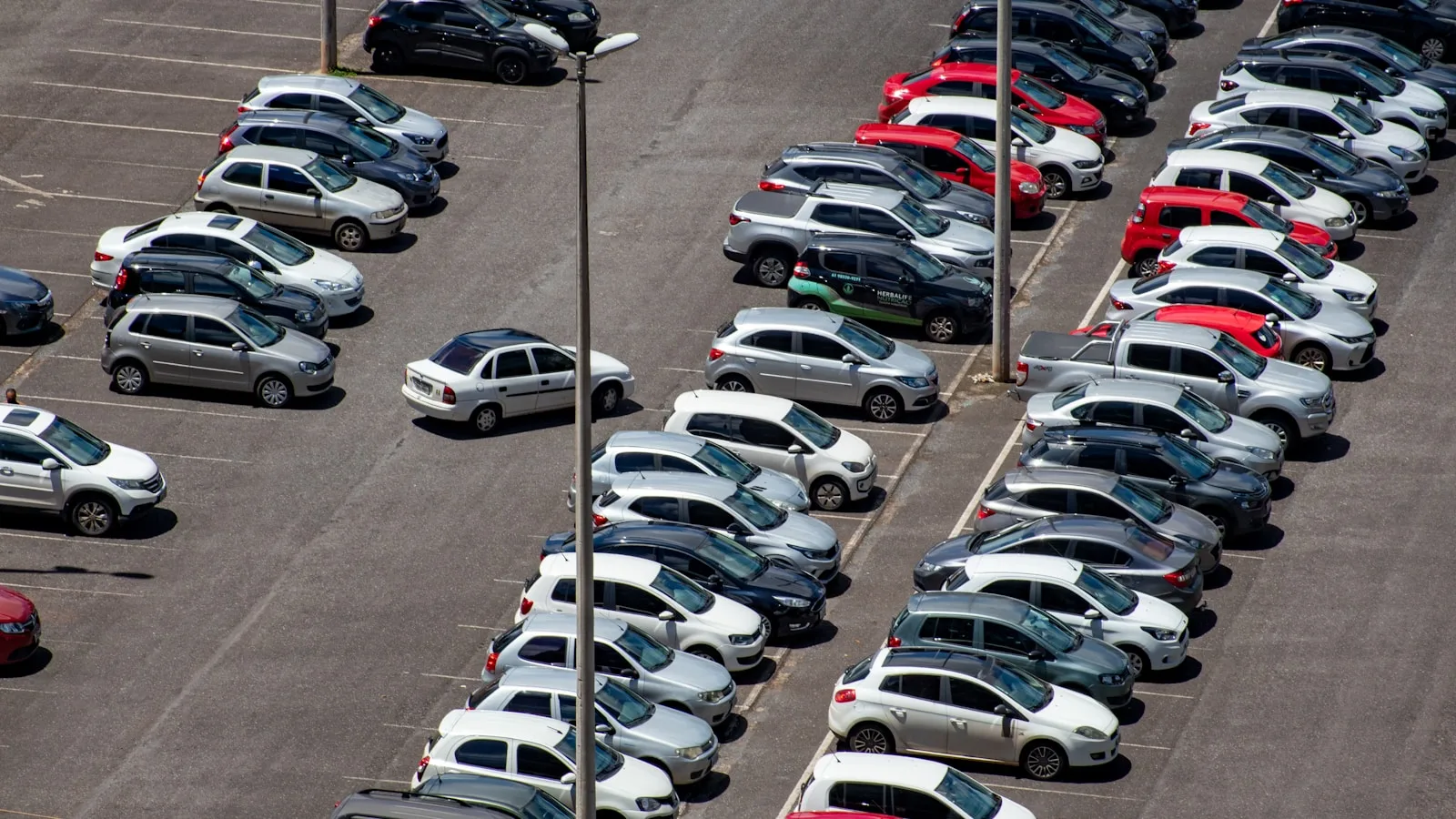 Vista aérea de un amplio aparcamiento exterior con múltiples coches estacionados en filas ordenadas sobre asfalto.