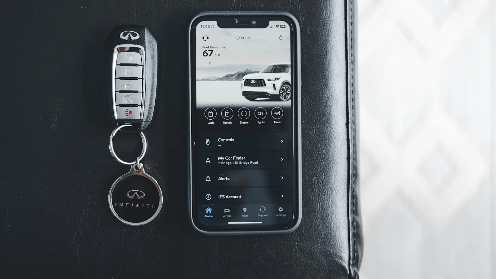 Llave de coche Infiniti junto a un smartphone que muestra la app del vehículo con controles remotos y alertas.