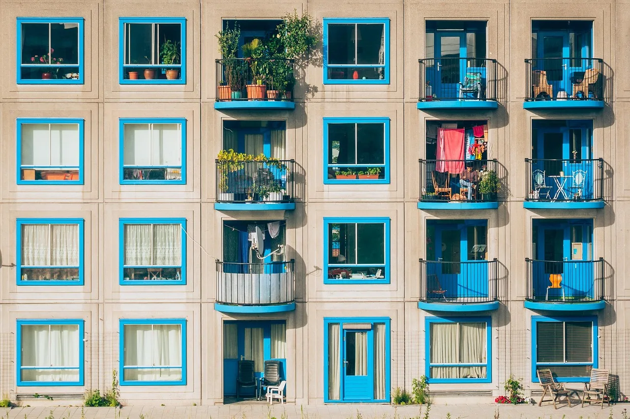 Fachada de edificio residencial con ventanas y balcones de marco azul intenso, algunos con plantas y objetos personales.