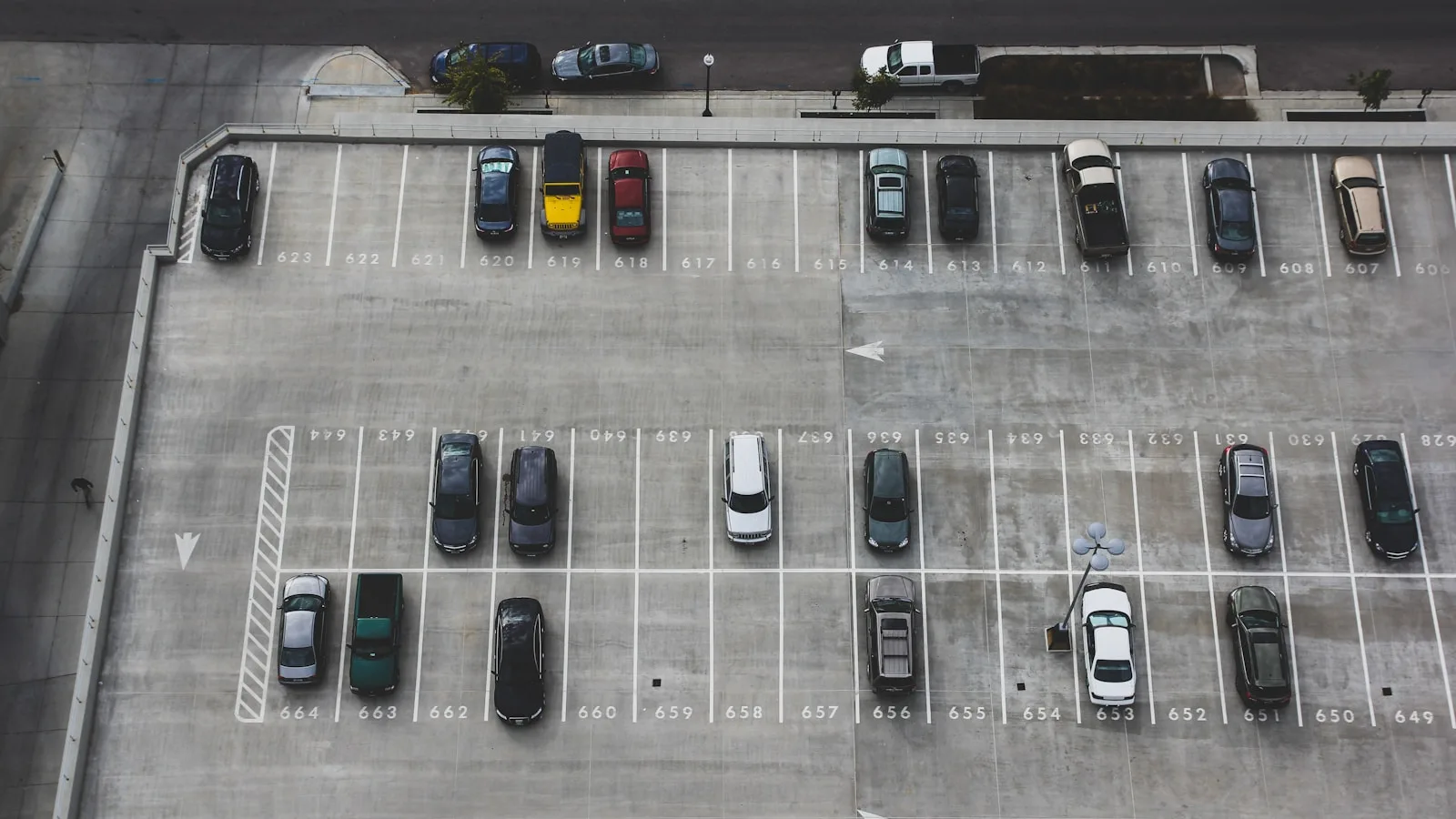 Vista aérea de un aparcamiento con múltiples coches estacionados en plazas numeradas y líneas blancas.