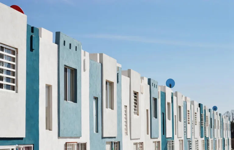 Fila de viviendas públicas de fachada blanca y azul bajo un cielo despejado