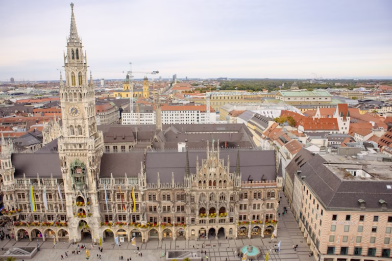 Vista aérea del Ayuntamiento de Múnich con su icónica torre gótica y la plaza Marienplatz llena de gente.
